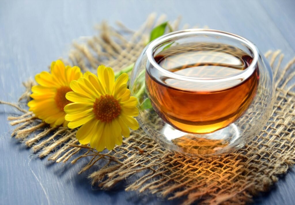 A glass cup of calendula tea with yellow flowers.