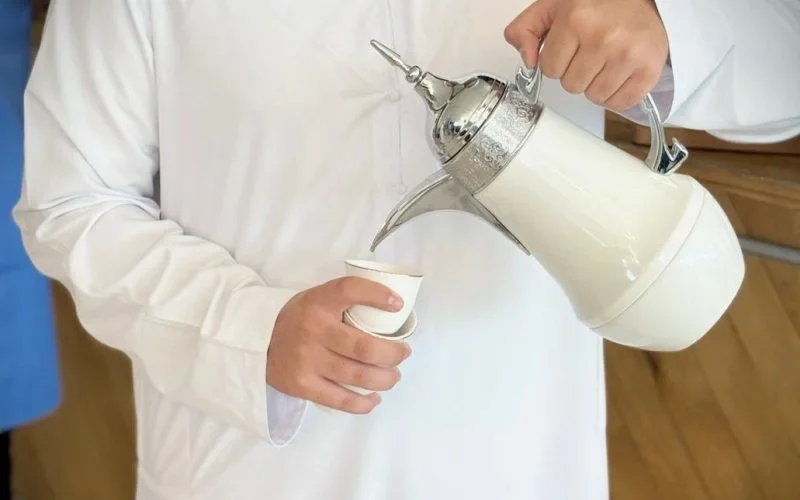 Person in traditional attire pouring Arabic coffee from a dallah