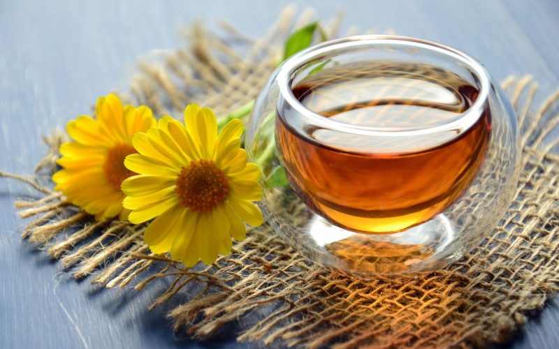 A glass cup of calendula tea with yellow flowers.